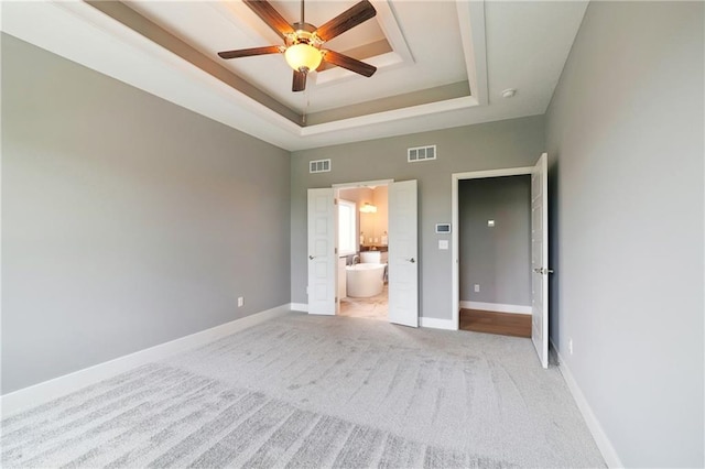 unfurnished bedroom with ceiling fan, connected bathroom, a tray ceiling, and light colored carpet