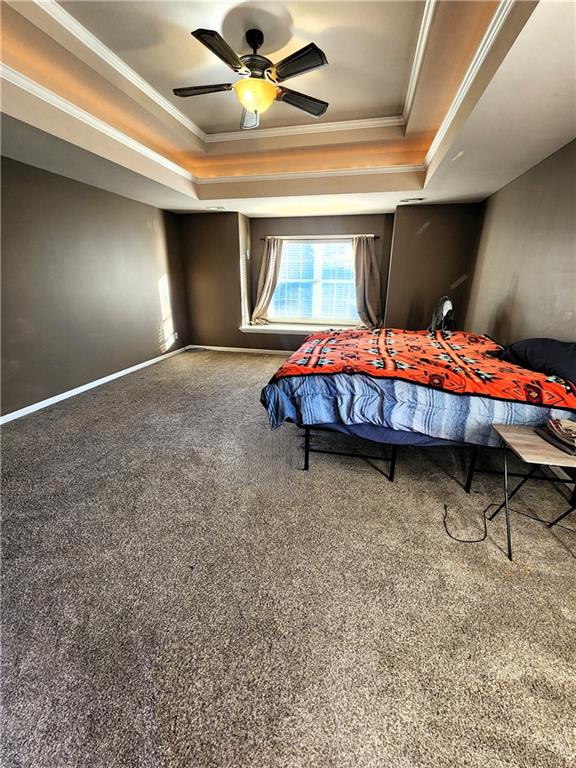 carpeted bedroom with ceiling fan, ornamental molding, and a tray ceiling