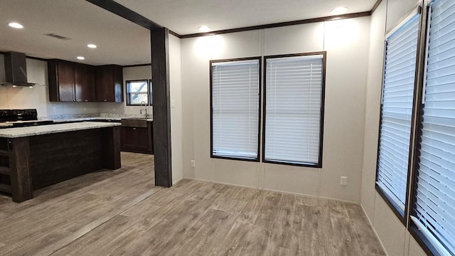 kitchen featuring ornamental molding, light hardwood / wood-style floors, dark brown cabinets, and wall chimney exhaust hood