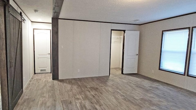 unfurnished bedroom with light hardwood / wood-style flooring, a barn door, a spacious closet, ornamental molding, and a closet