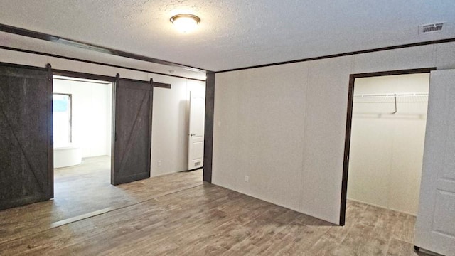 unfurnished bedroom with hardwood / wood-style floors, crown molding, a barn door, a textured ceiling, and a closet