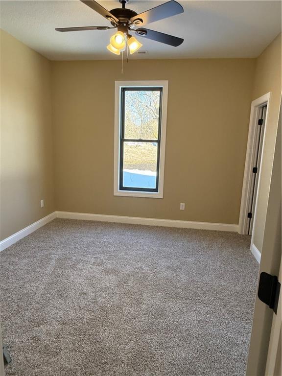 carpeted empty room featuring a ceiling fan and baseboards