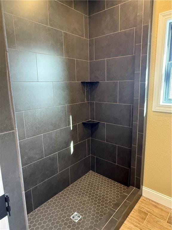 full bath featuring wood tiled floor, a tile shower, and baseboards