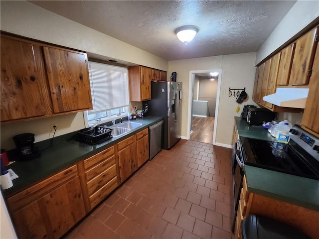 2716 N 10th St, Independence, KS 67301 - kitchen featuring appliances with stainless steel finishes, under cabinet range hood, a textured ceiling, brown cabinetry, and dark countertops