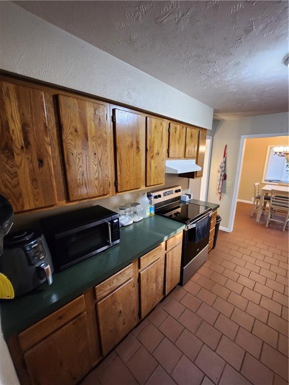 2716 N 10th St, Independence, KS 67301 - kitchen featuring stainless steel electric stove, under cabinet range hood, brown cabinetry, a textured ceiling, and dark countertops