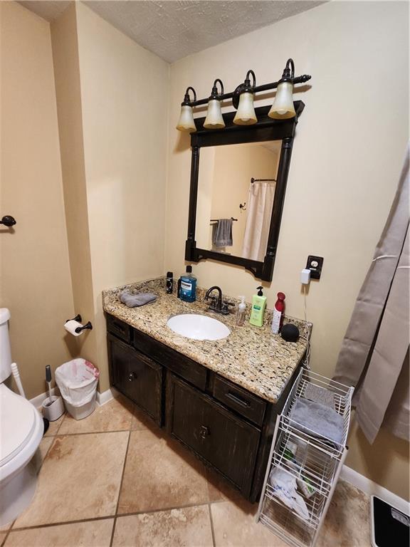 2716 N 10th St, Independence, KS 67301 - bathroom featuring toilet, vanity, baseboards, a textured ceiling, and tile patterned floors