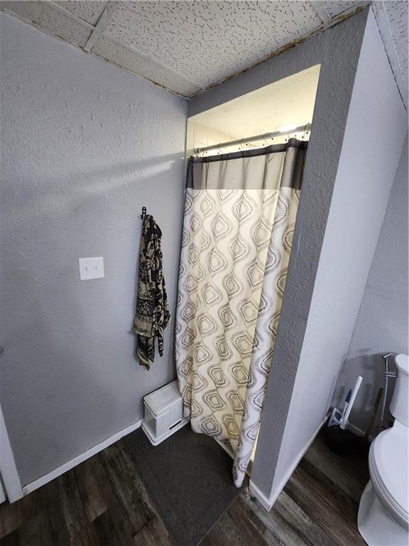 2716 N 10th St, Independence, KS 67301 - bathroom featuring wood finished floors, toilet, a shower with curtain, a textured wall, and baseboards