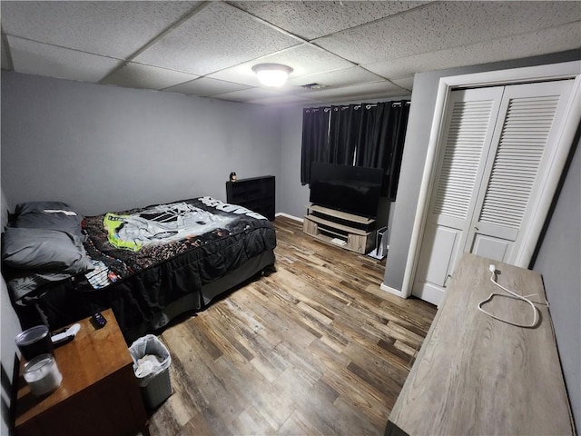 bedroom with a drop ceiling, hardwood / wood-style floors, and a closet