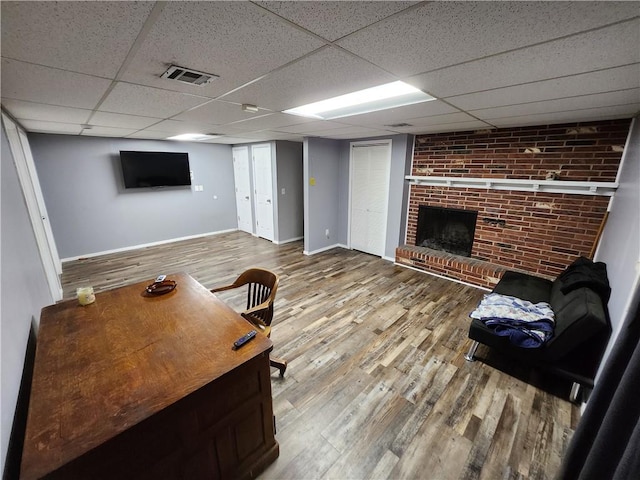 unfurnished living room featuring a brick fireplace, hardwood / wood-style flooring, brick wall, and a drop ceiling