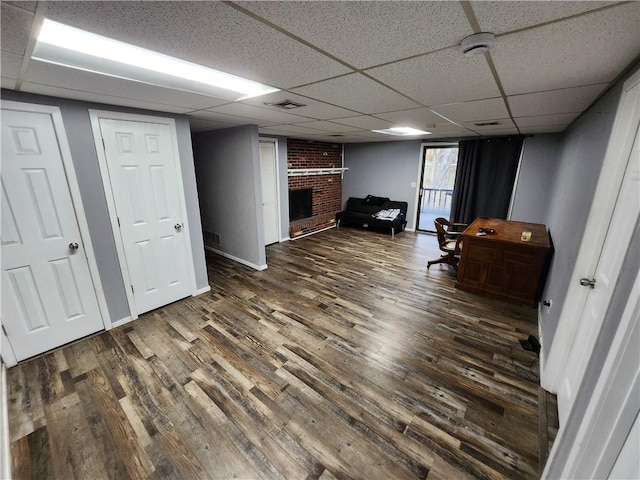 interior space with a brick fireplace, a paneled ceiling, and dark hardwood / wood-style floors