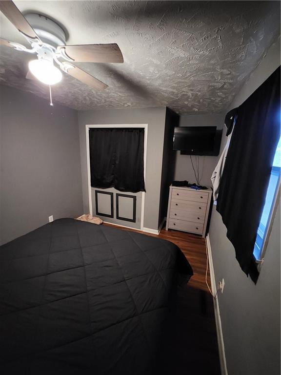 bedroom with a textured ceiling, ceiling fan, and dark hardwood / wood-style floors