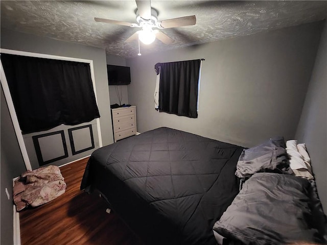 bedroom featuring dark wood-type flooring, a textured ceiling, and ceiling fan