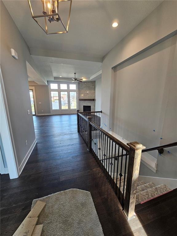 stairway with a large fireplace, wood-type flooring, and ceiling fan with notable chandelier