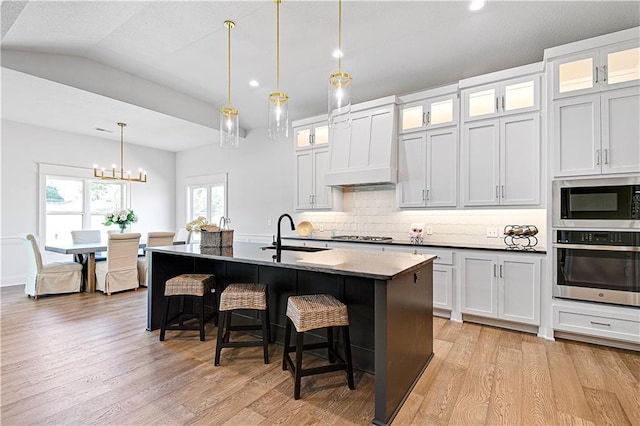 24912 W 98th Pl, Lenexa, KS 66227 - kitchen with stainless steel appliances, a sink, custom range hood, a kitchen breakfast bar, and light wood-style flooring