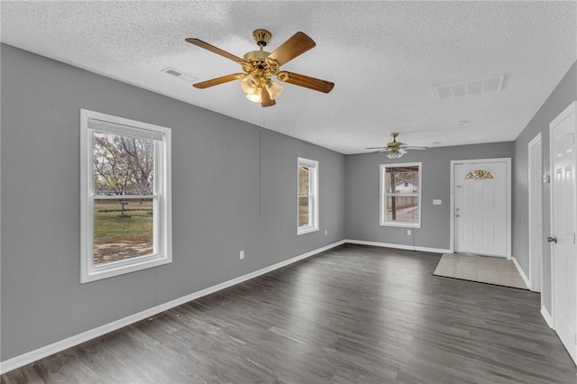 interior space featuring a healthy amount of sunlight, ceiling fan, dark wood-type flooring, and a textured ceiling