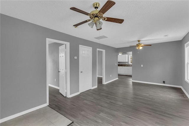 unfurnished living room with a wealth of natural light, ceiling fan, dark wood-type flooring, and a textured ceiling