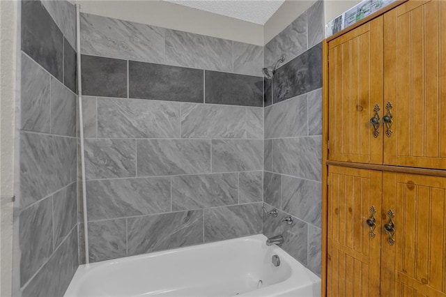 bathroom with a textured ceiling and tiled shower / bath