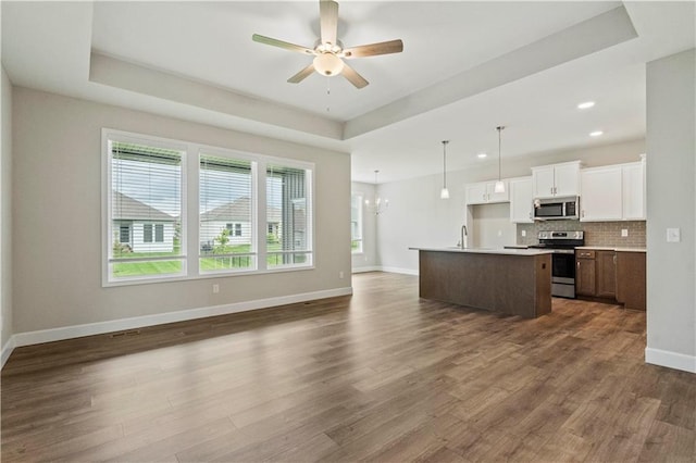 kitchen featuring stainless steel appliances, dark hardwood / wood-style flooring, an island with sink, white cabinets, and a tray ceiling