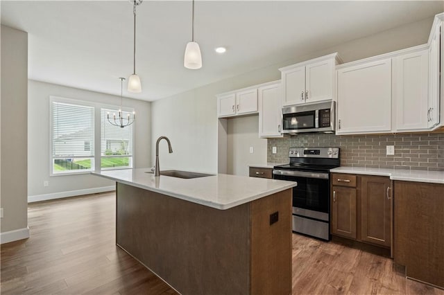 kitchen with stainless steel appliances, decorative light fixtures, sink, an island with sink, and white cabinets