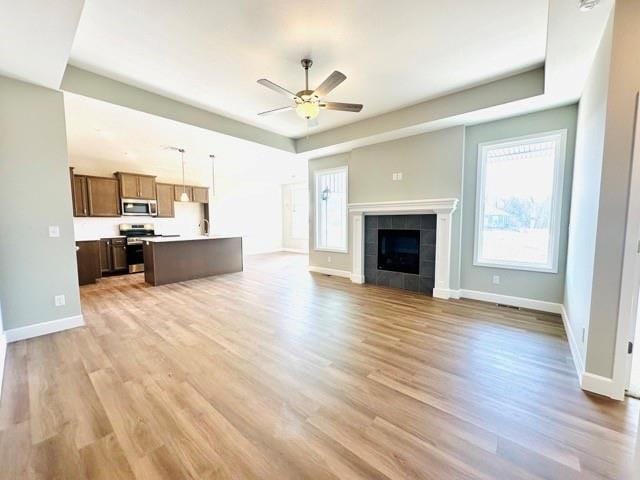 unfurnished living room featuring ceiling fan, light wood-type flooring, and a fireplace