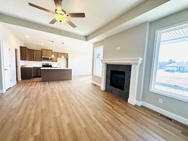 unfurnished living room with ceiling fan, a tiled fireplace, and hardwood / wood-style floors