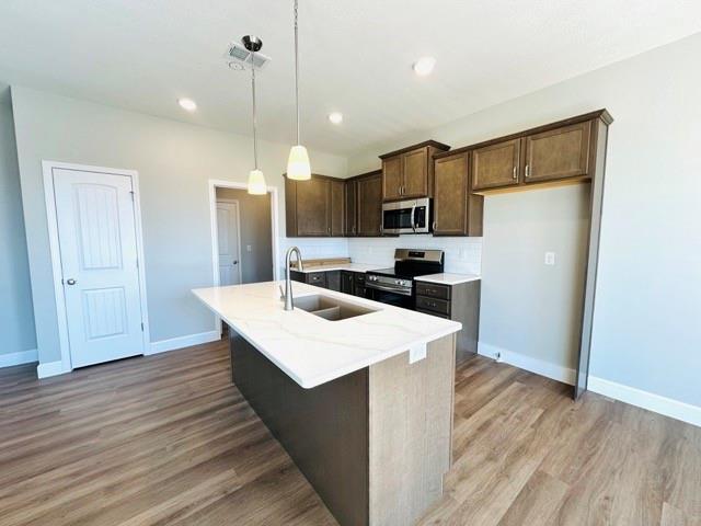 kitchen with sink, appliances with stainless steel finishes, hanging light fixtures, wood-type flooring, and a center island with sink