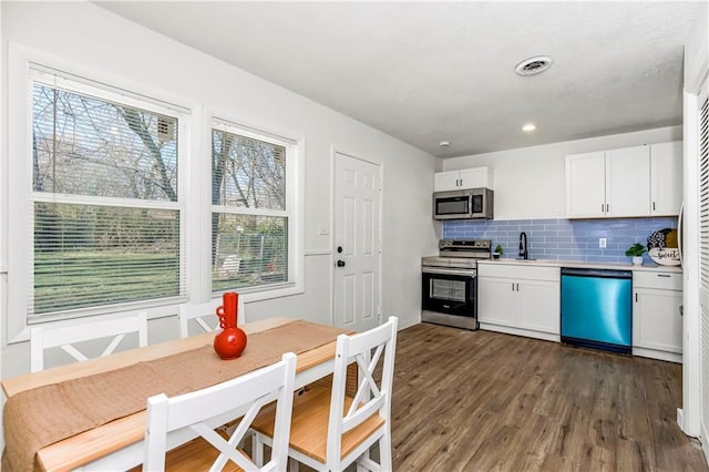 kitchen featuring dark hardwood / wood-style flooring, stainless steel appliances, white cabinetry, and a wealth of natural light