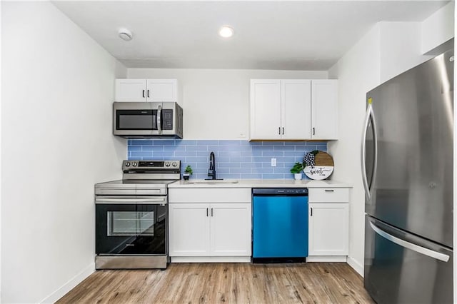 kitchen featuring decorative backsplash, appliances with stainless steel finishes, sink, light hardwood / wood-style flooring, and white cabinetry