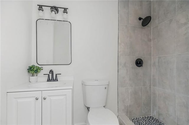 bathroom with a tile shower, vanity, and toilet