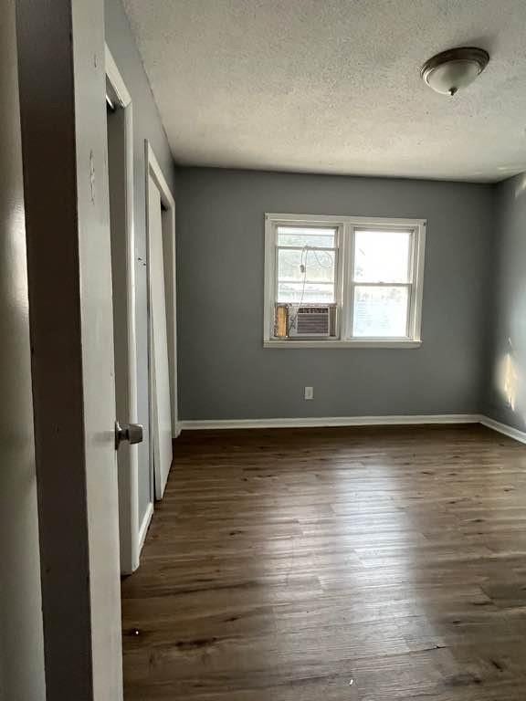 unfurnished bedroom with a textured ceiling, dark hardwood / wood-style floors, and cooling unit