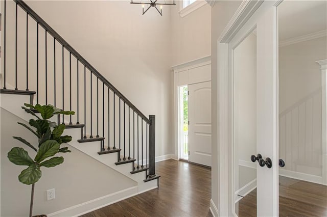 entrance foyer with dark wood-type flooring, a high ceiling, a chandelier, and ornamental molding