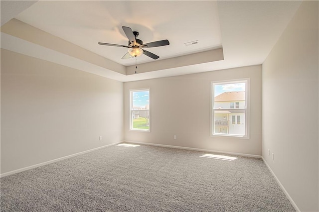 carpeted empty room with a wealth of natural light, ceiling fan, and a tray ceiling