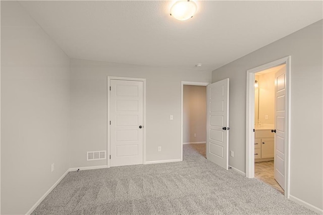 unfurnished bedroom featuring a closet, light colored carpet, and connected bathroom