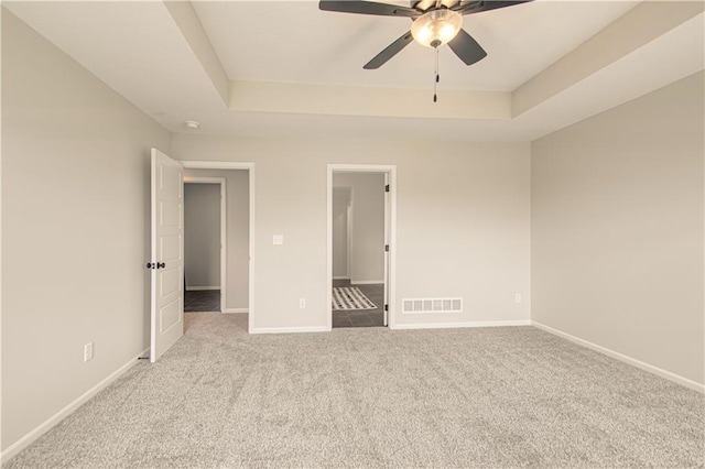 unfurnished bedroom with light colored carpet, ceiling fan, and a raised ceiling