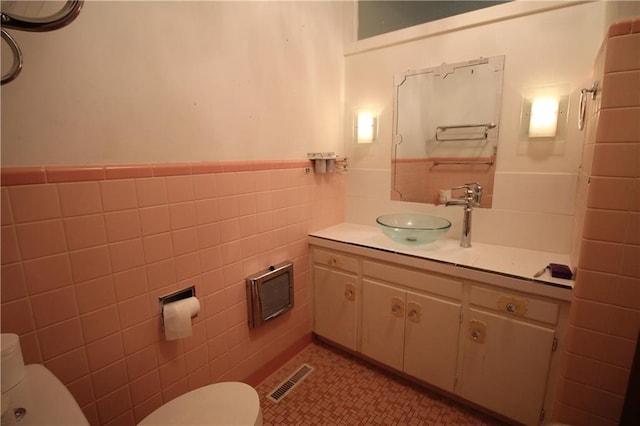 bathroom with toilet, vanity, and tile walls