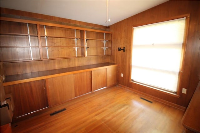 interior space with light hardwood / wood-style flooring, wood walls, lofted ceiling, and plenty of natural light