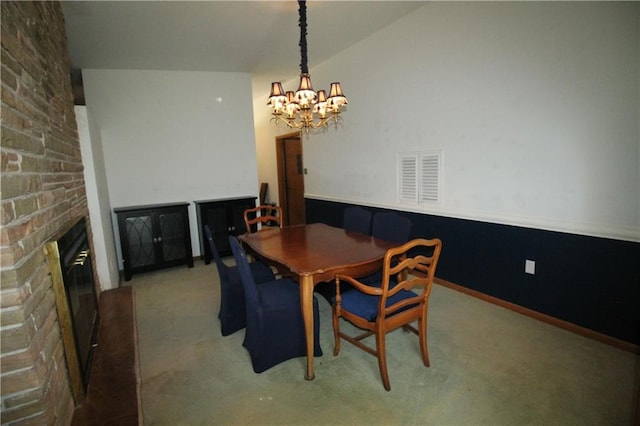 carpeted dining room featuring a chandelier, a stone fireplace, and vaulted ceiling