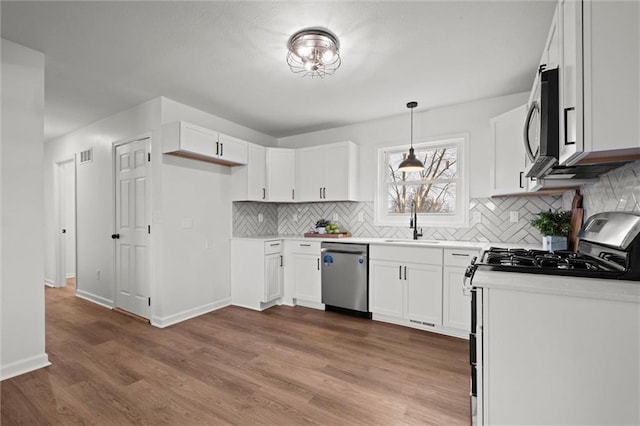 kitchen featuring hardwood / wood-style floors, decorative light fixtures, white cabinetry, and stainless steel appliances