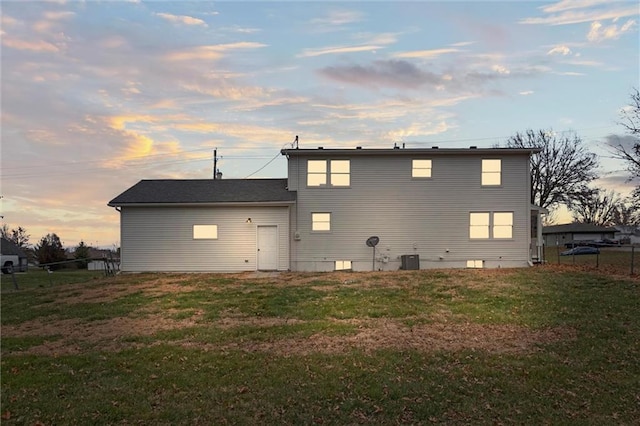 back house at dusk featuring central air condition unit and a lawn