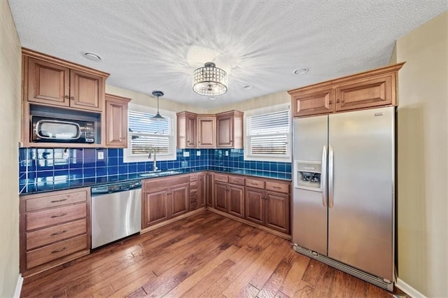 kitchen with pendant lighting, sink, hardwood / wood-style flooring, appliances with stainless steel finishes, and tasteful backsplash