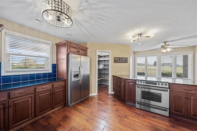 kitchen featuring tasteful backsplash, dark hardwood / wood-style flooring, a textured ceiling, ceiling fan with notable chandelier, and appliances with stainless steel finishes