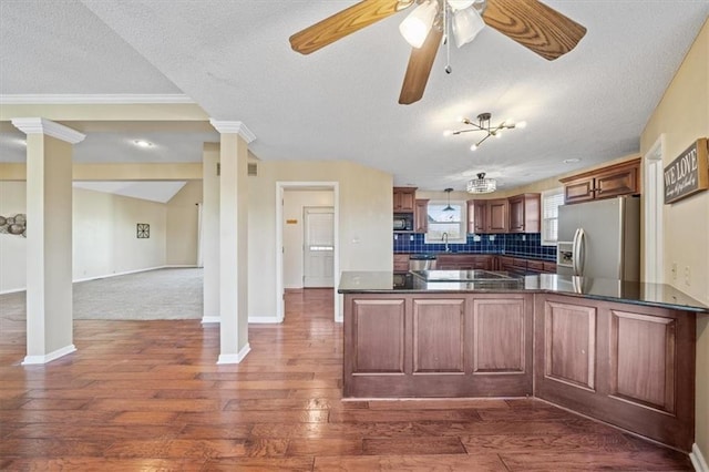 kitchen with dark wood-type flooring, a textured ceiling, tasteful backsplash, kitchen peninsula, and stainless steel appliances