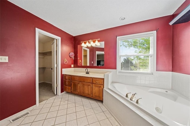 bathroom featuring tile patterned floors, vanity, a textured ceiling, and tiled tub