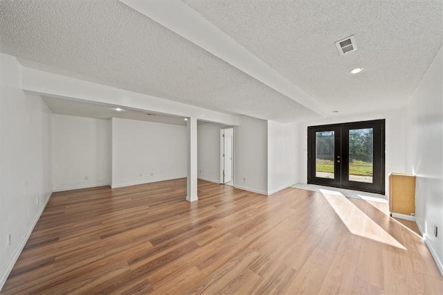 basement with a textured ceiling, light wood-type flooring, and french doors