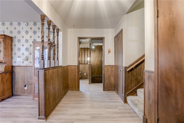 corridor with wood walls, light hardwood / wood-style floors, and a textured ceiling