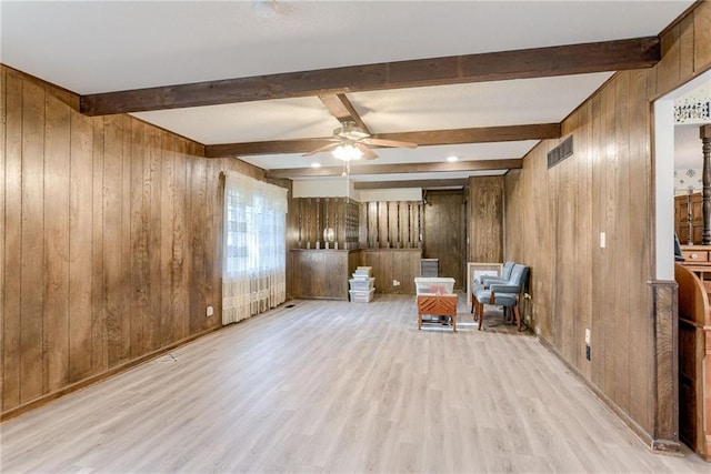 unfurnished room with beam ceiling, light hardwood / wood-style flooring, ceiling fan, and wood walls