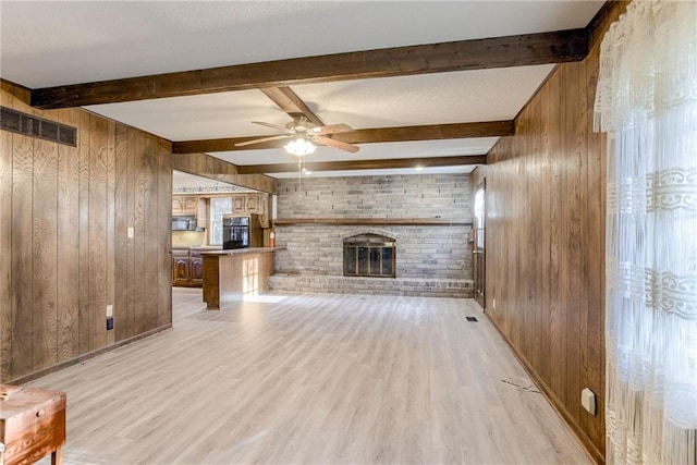 unfurnished living room featuring beam ceiling, wooden walls, and light hardwood / wood-style flooring