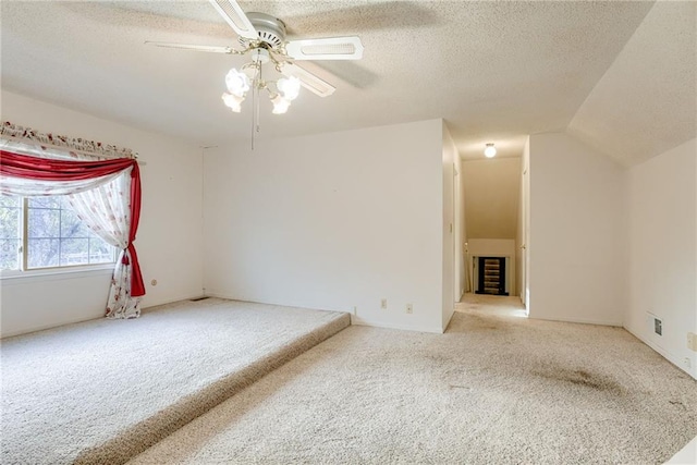 spare room featuring vaulted ceiling, ceiling fan, light carpet, and a textured ceiling