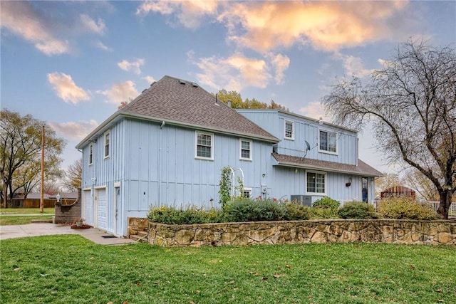 back house at dusk featuring a lawn and a garage