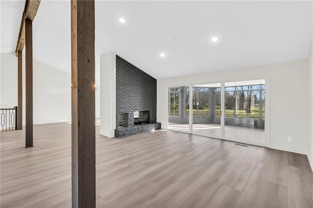 unfurnished living room featuring a brick fireplace, light hardwood / wood-style flooring, and vaulted ceiling